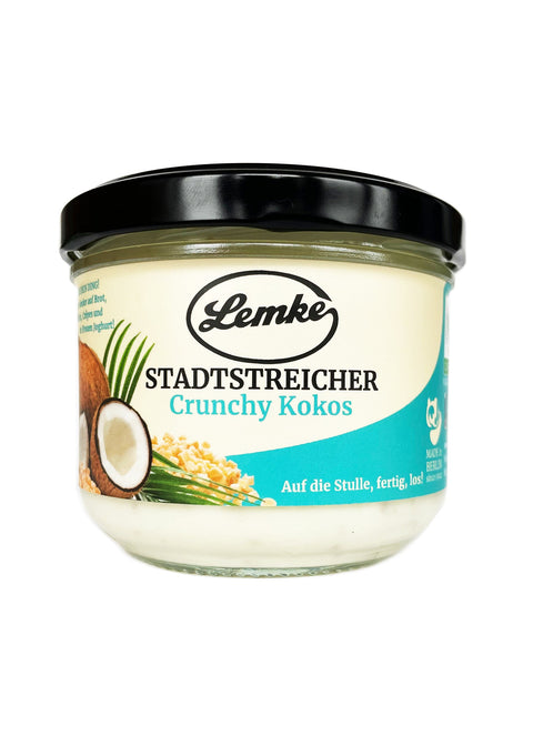 Ein Glas Lemke Stadtstreicher Crunchy Kokoscreme mit schwarzem Deckel, einer Kokosnuss und knusprigem Getreide auf dem Etikett, ideal als Aufstrich oder Zutat in Rezepten für Desserts und vegane Gerichte.
